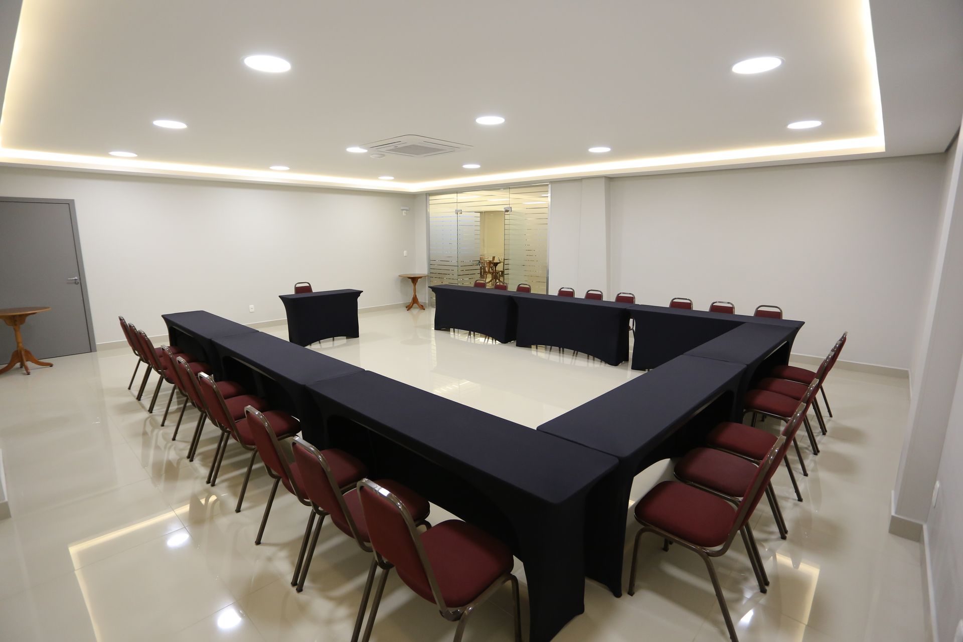 Hall de entrada do hotel com balcão de recepção em madeira marrom, pilares e piso branco brilhante.