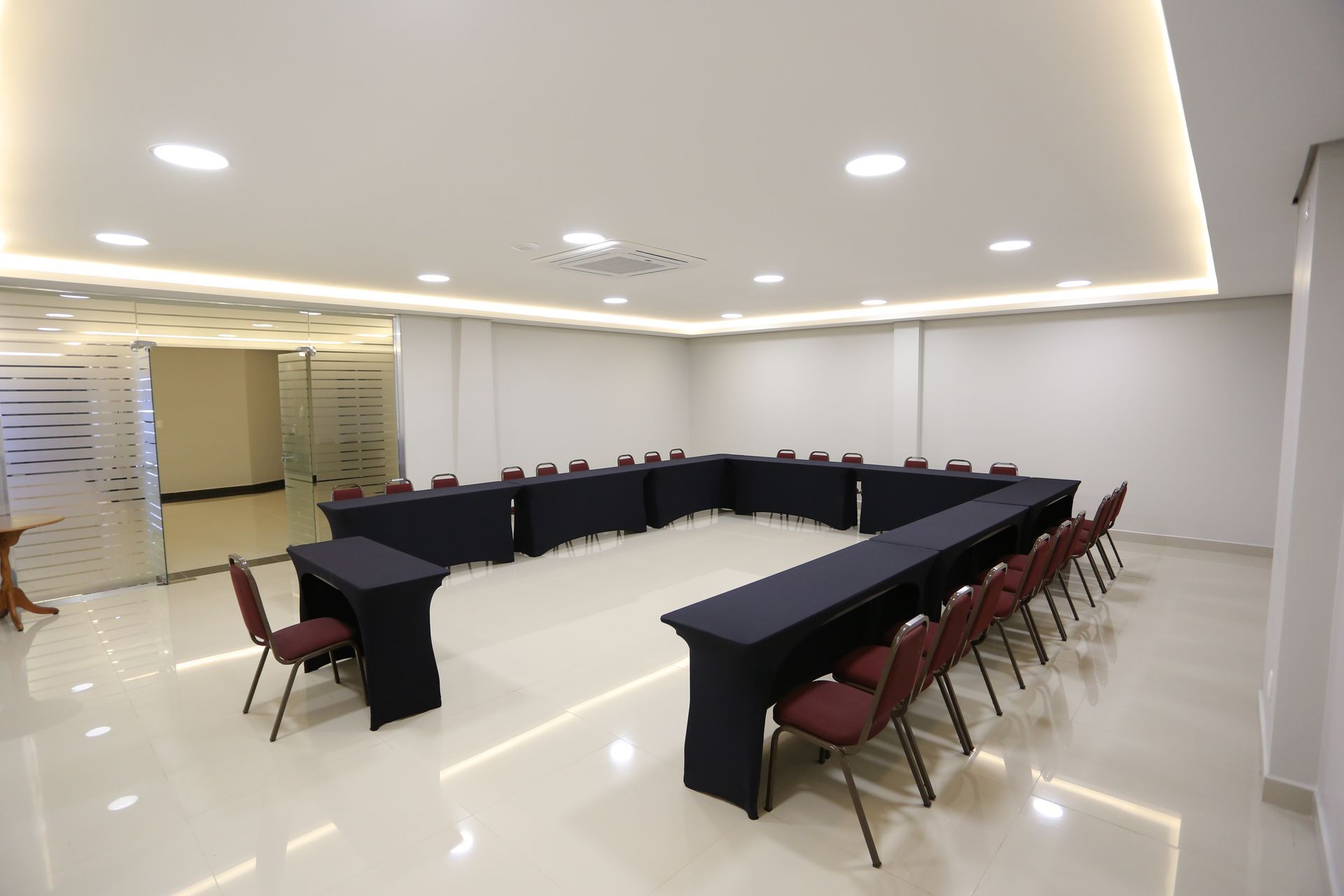 Sala de conferências vazia com fileiras de cadeiras cinzentas voltadas para a parede frontal.