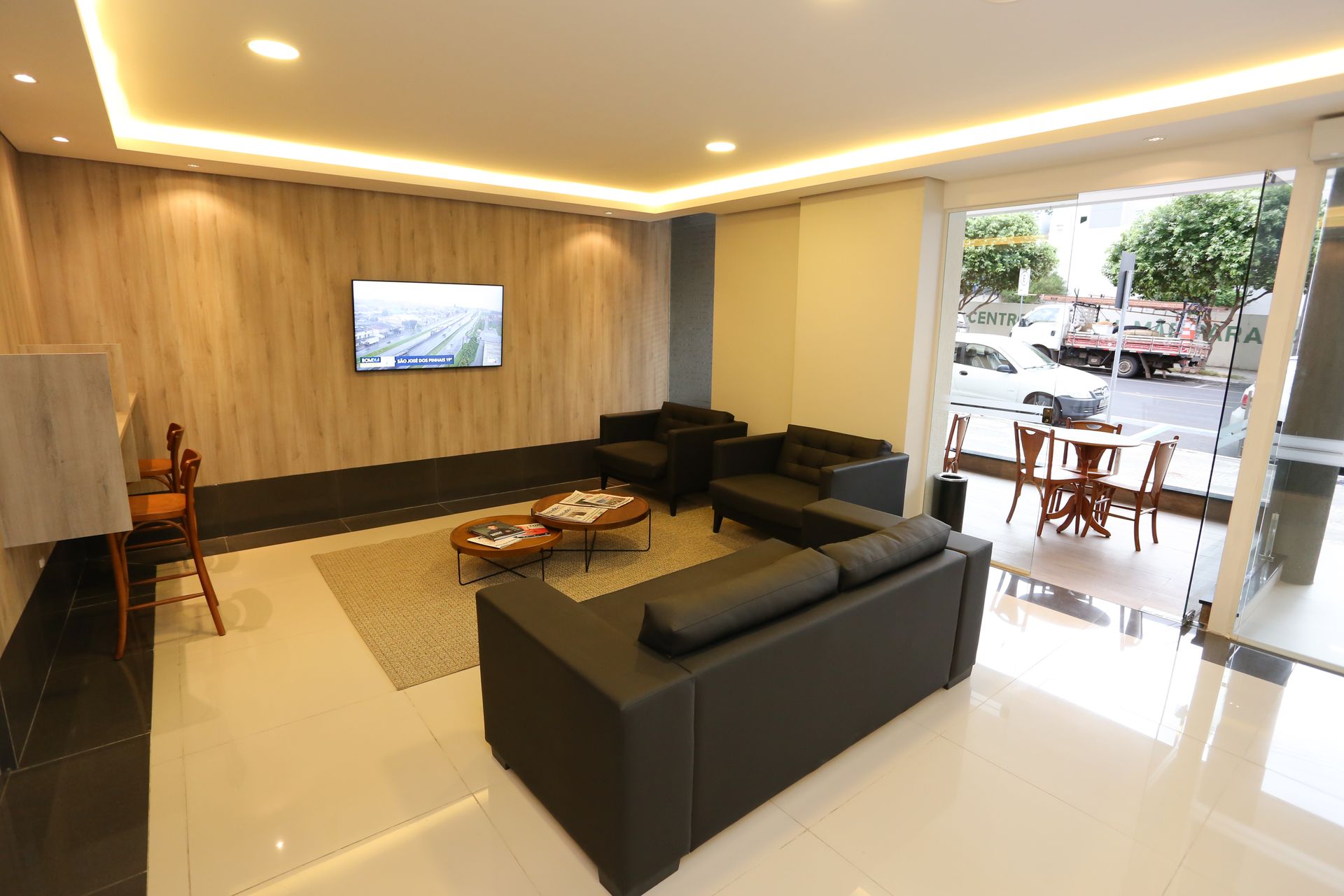 Sala de conferências com mesas dispostas em forma de U, cadeiras vermelhas, tela de projeção e piso de madeira.