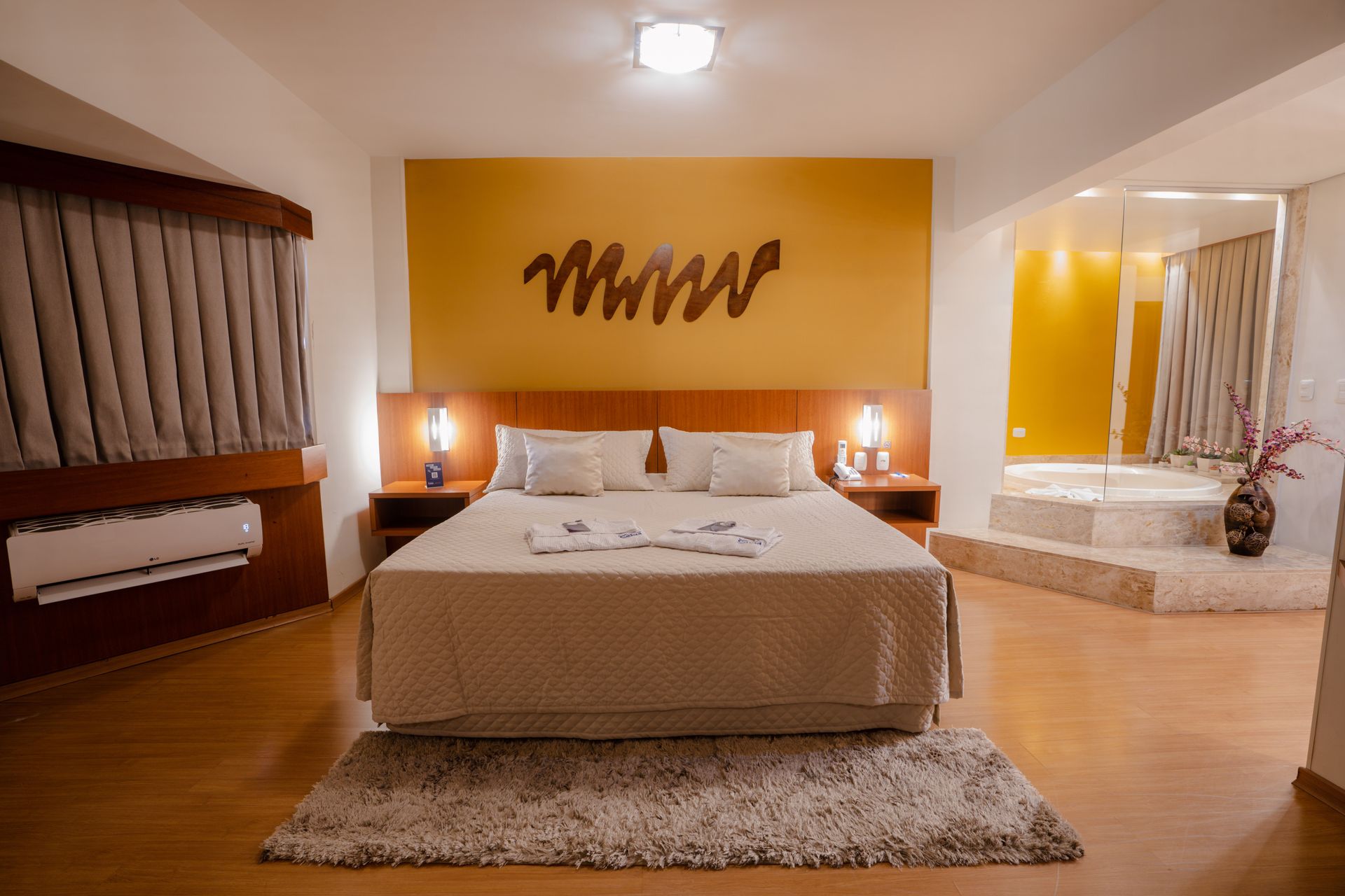 Quarto com cama, mesas de cabeceira, jacuzzi e paredes bege.