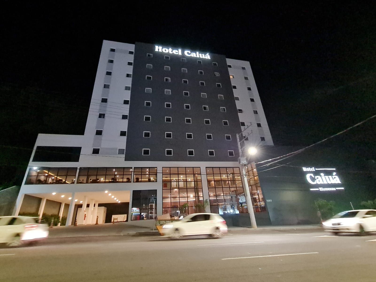 O Hotel Caluá à noite, um moderno edifício de vários andares com janelas iluminadas e carros na rua.