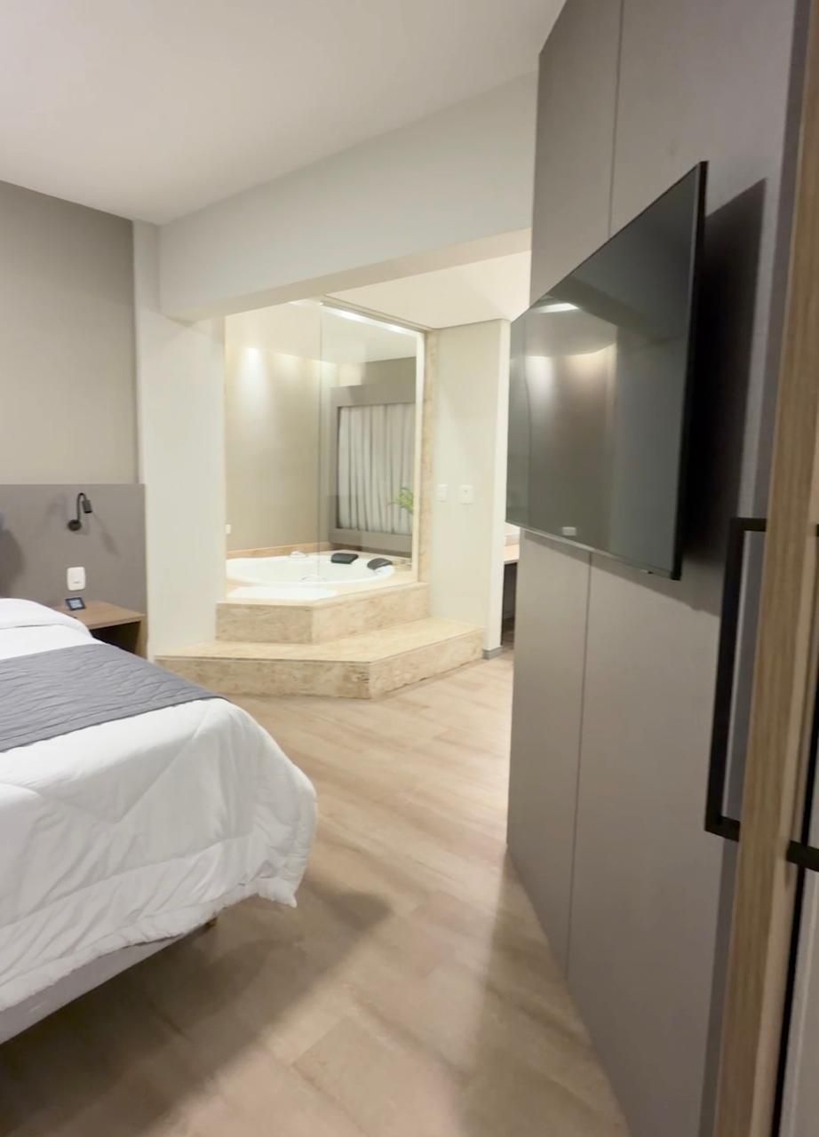 Quarto de hotel com duas camas de solteiro, escrivaninha e TV. Decoração em tons de marrom claro e bege.