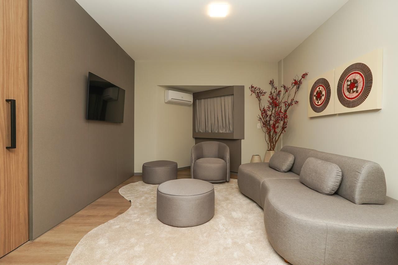 Suíte Presidencial com Sala de estar moderna com sofá modular cinza, pufes redondos, TV de parede e decoração em tons neutros suaves.