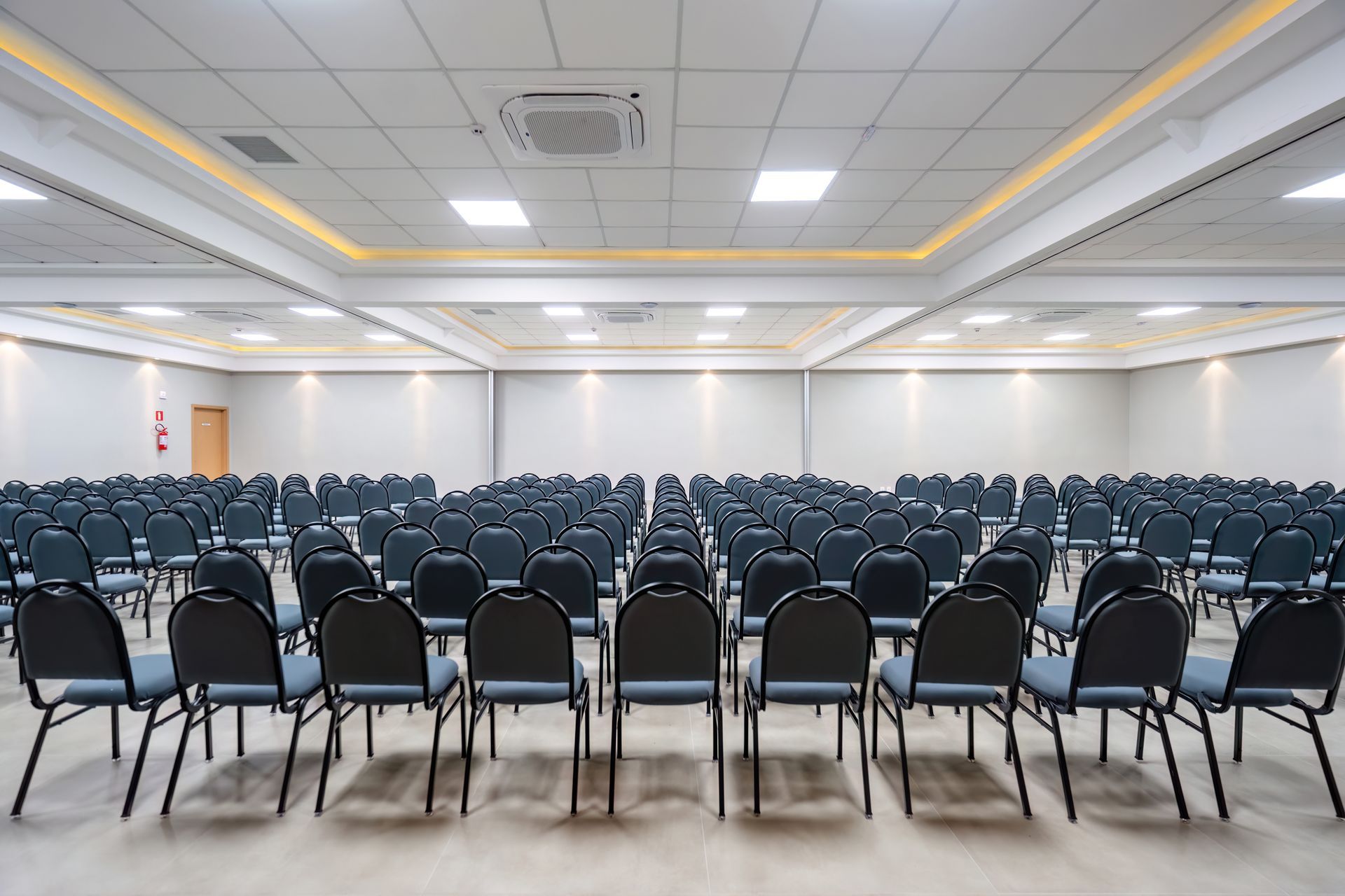 Sala de conferências vazia com fileiras de cadeiras cinzentas voltadas para a parede frontal.