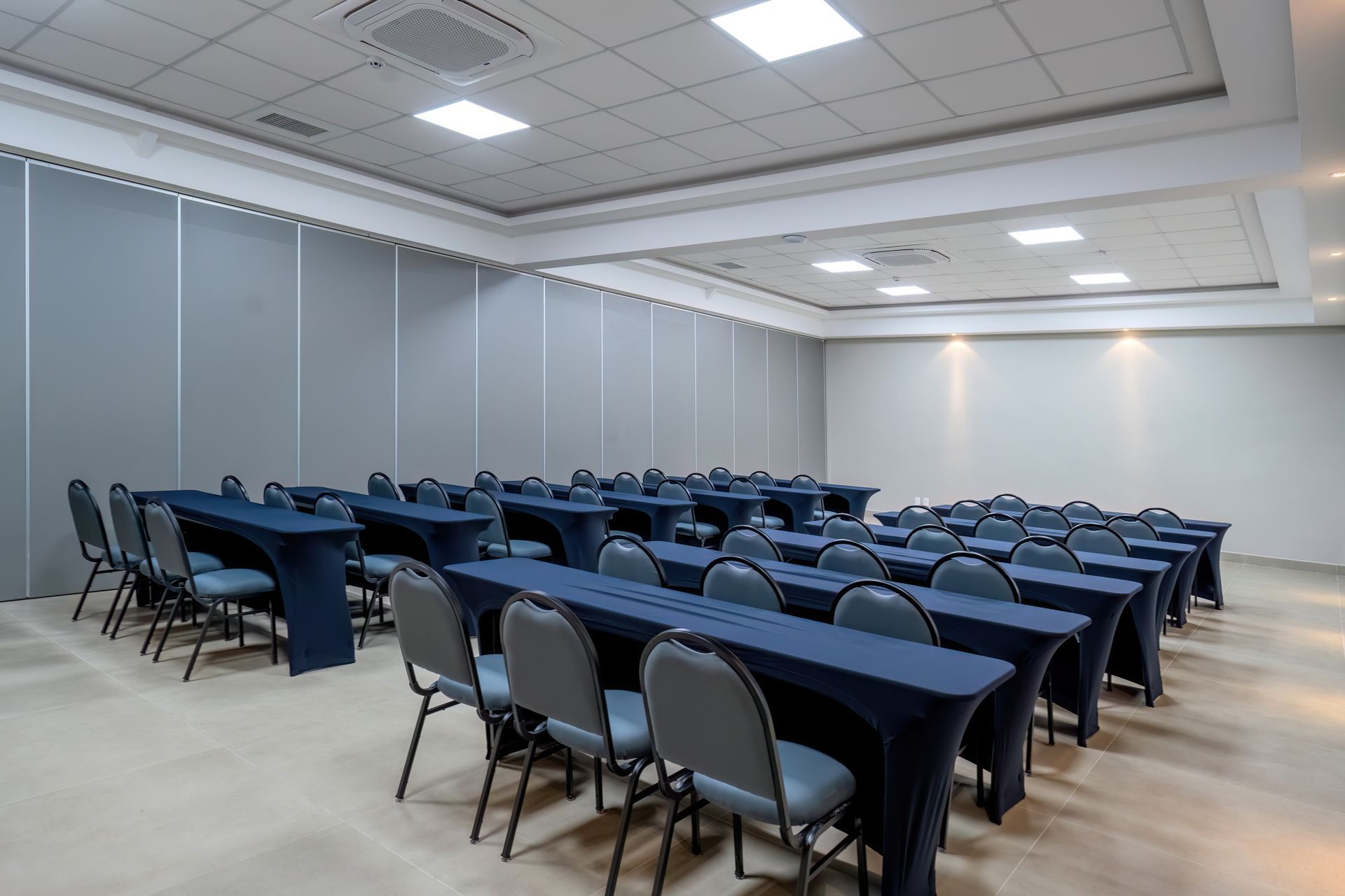 Sala de conferências com fileiras de mesas e cadeiras, toalhas de mesa azuis.