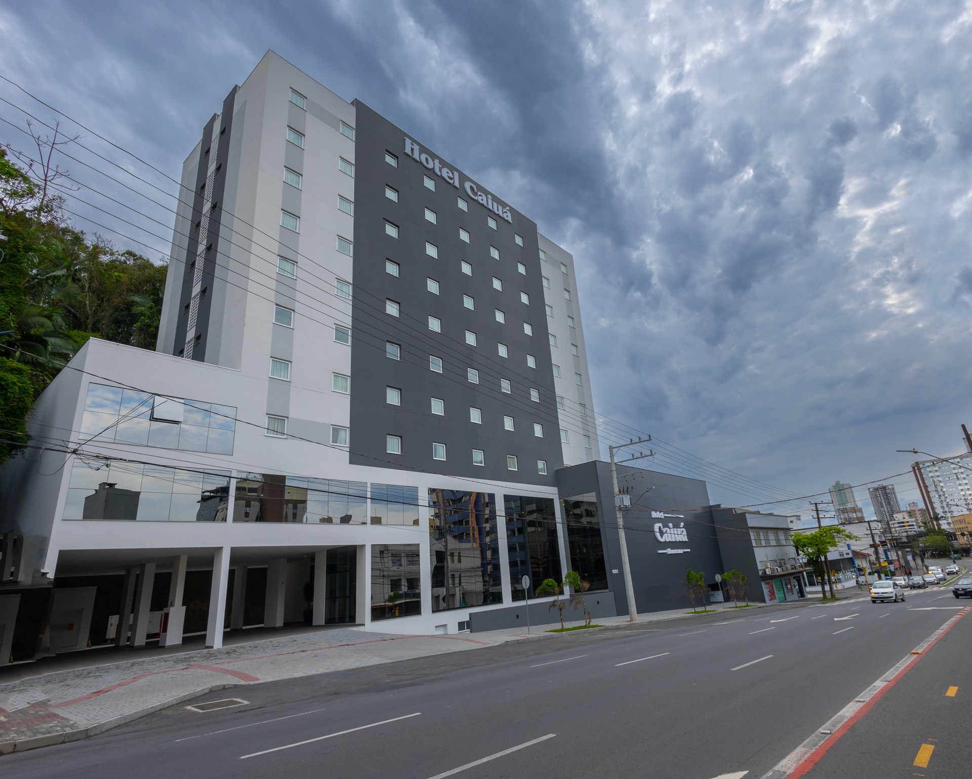 Quarto de hotel com três camas, janela com cortinas e iluminação aconchegante.