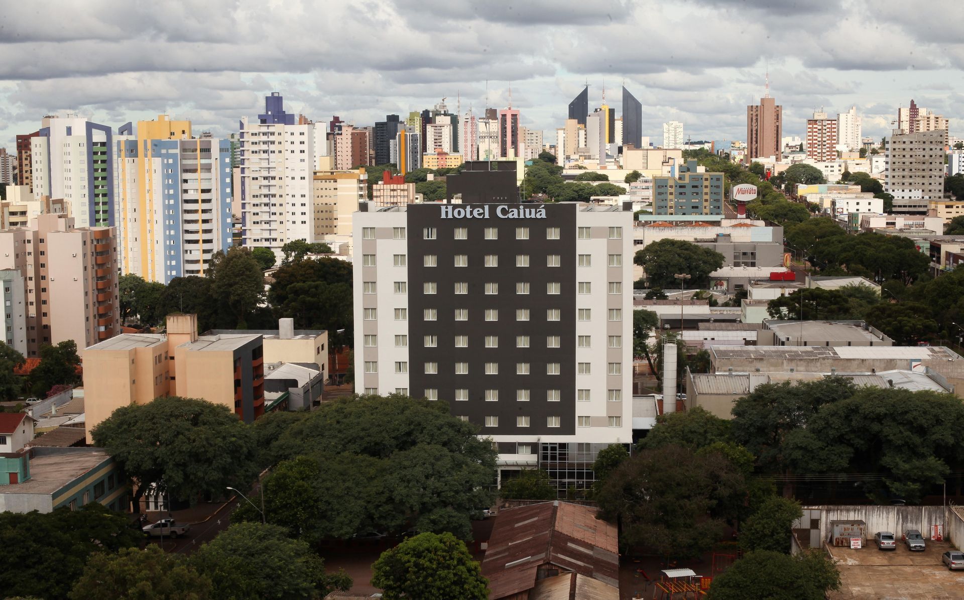 Hotel com a placa “Hotel Caiá” em frente a um horizonte urbano com prédios e árvores.