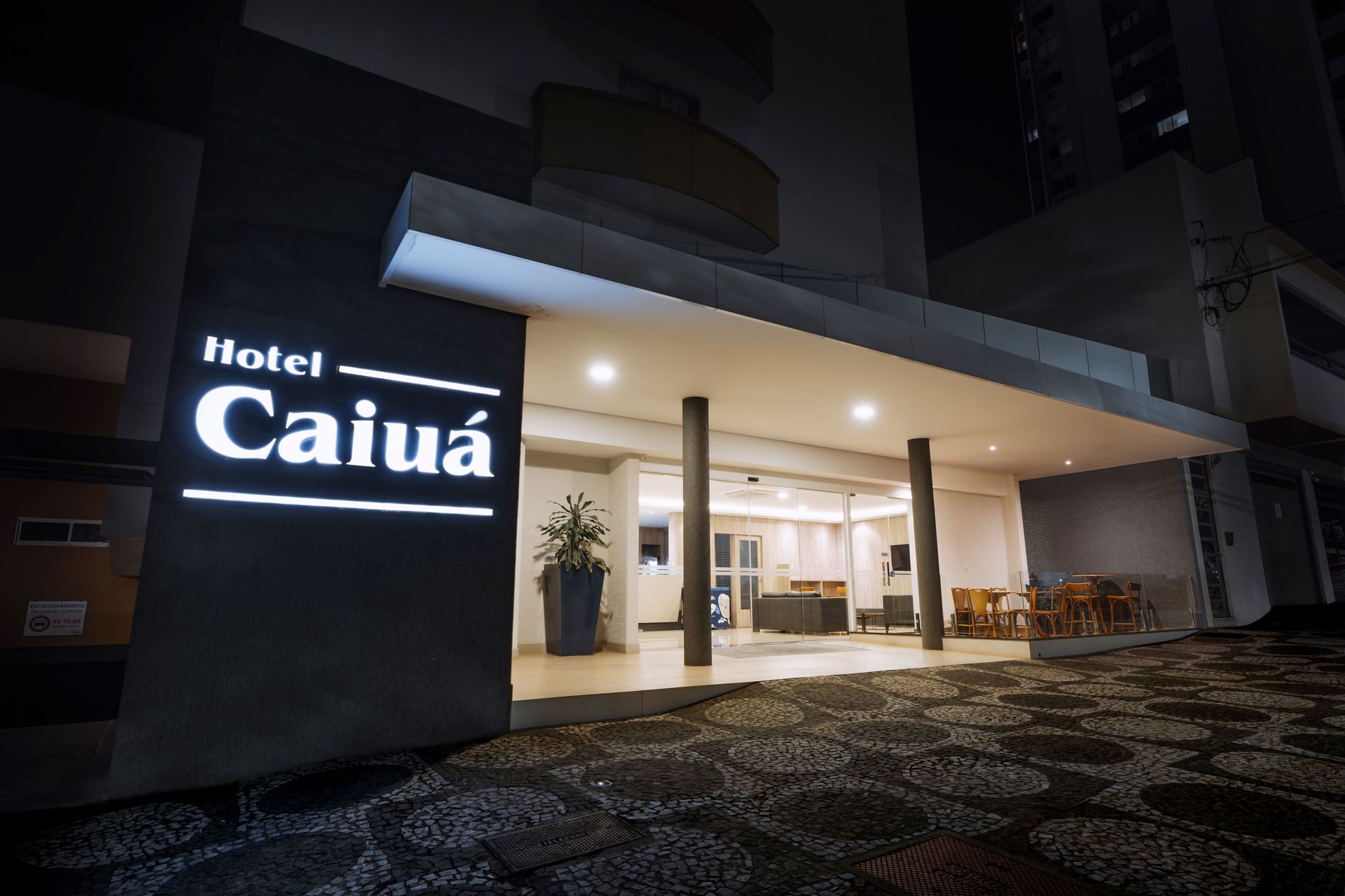 Entrada do Hotel Caiuá iluminada à noite. Exterior escuro com placa.