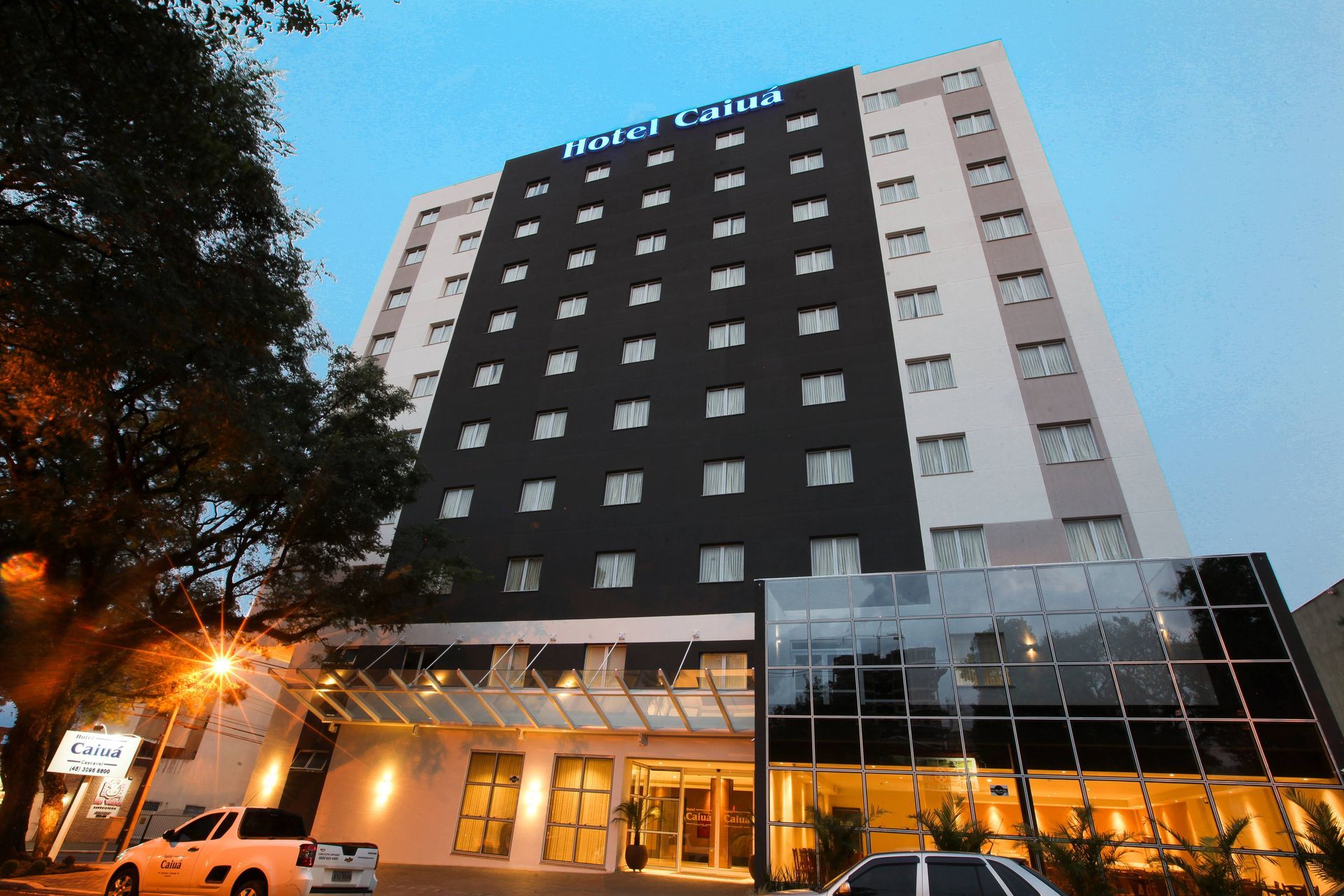 Exterior do Hotel Colina, prédio alto, fachada em preto e branco, entrada de vidro, postes de iluminação.