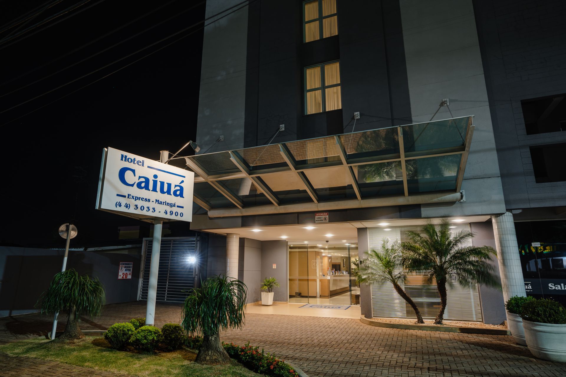 Hall de entrada com áreas de estar: sofás, poltronas e mesas redondas. Elevador e grandes janelas ao fundo.