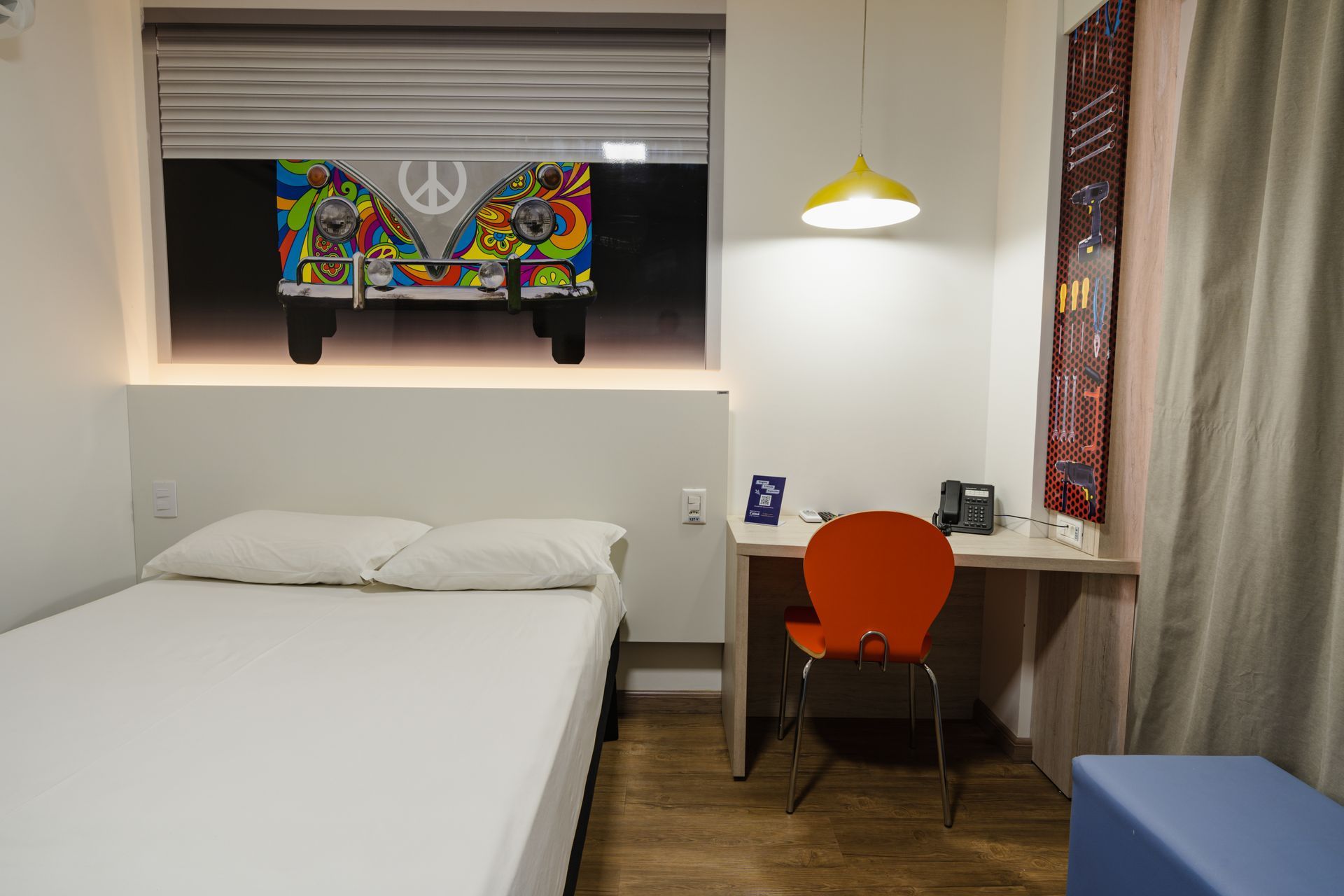 Quarto com cama king-size, porta de correr para o banheiro com azulejos vermelhos, dois abajures e obras de arte na parede.