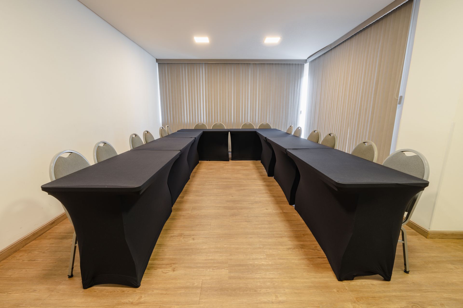 Sala de conferências com mesas dispostas em forma de U, cadeiras vermelhas, tela de projeção e piso de madeira.