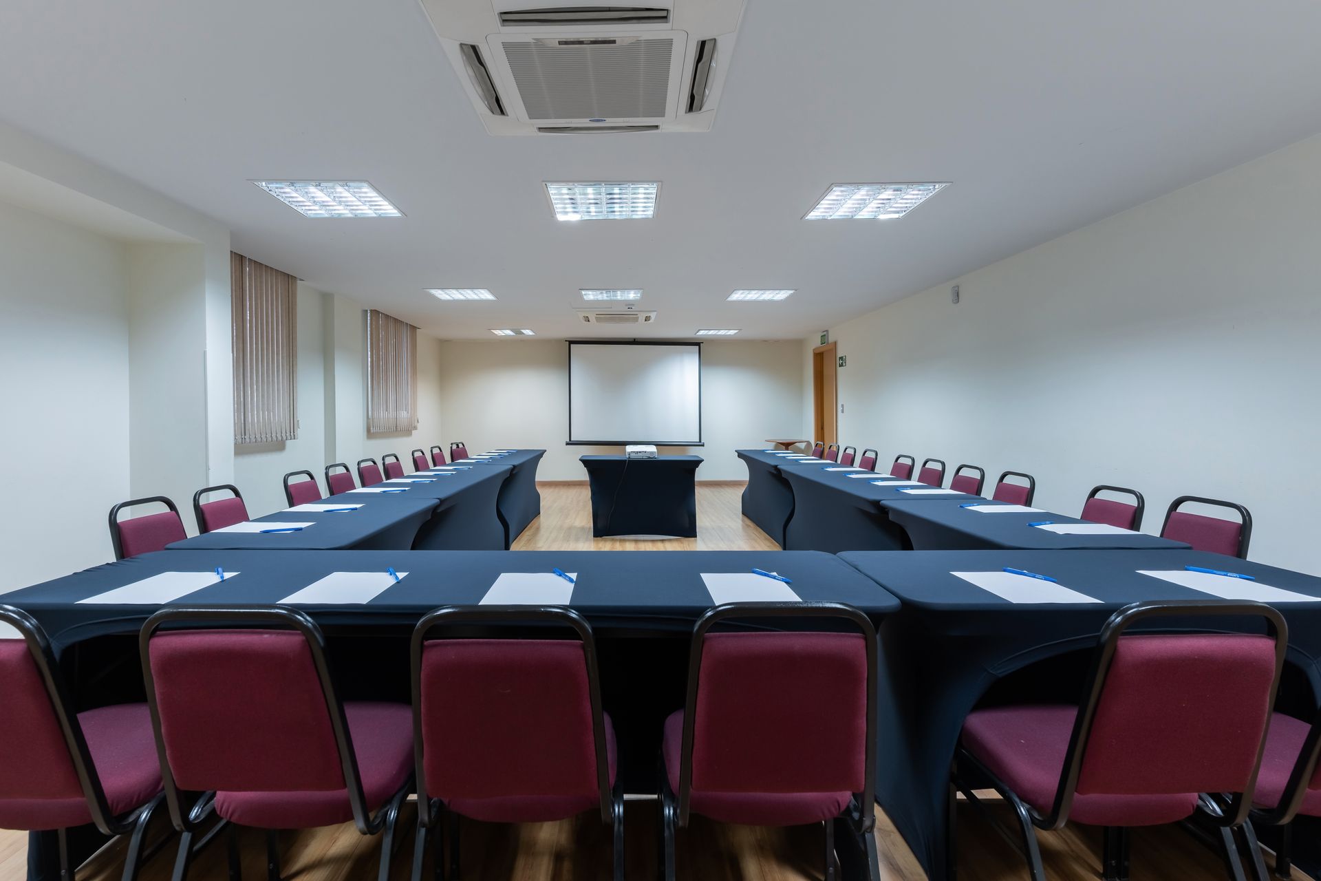 Sala de conferências preparada para uma reunião, com mesas dispostas em forma de U e cadeiras.