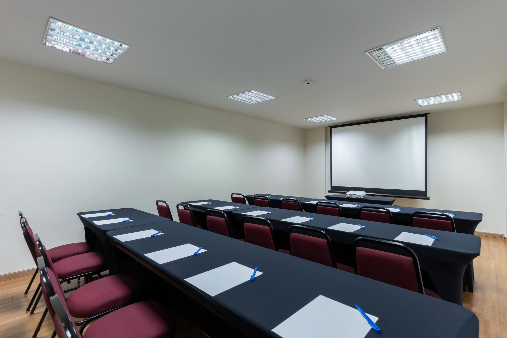 Sala de conferências vazia com fileiras de mesas cobertas com toalhas pretas.