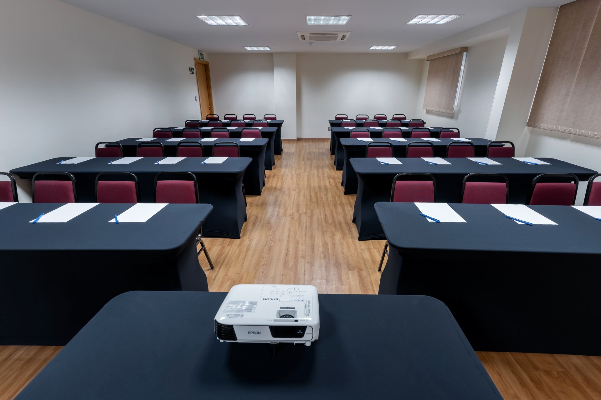 Uma sala de conferências com mesas e cadeiras, um projetor e papéis.