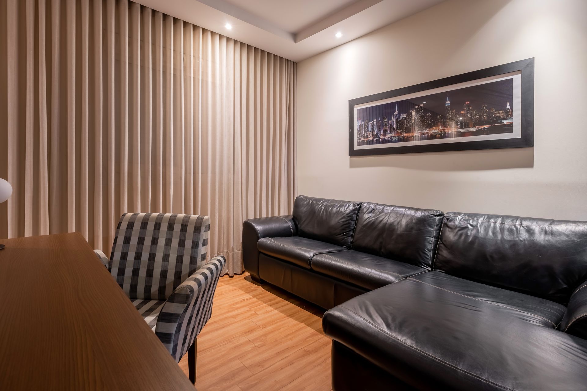 Sala de estar com sofá modular de couro preto, poltrona listrada e cortinas em tons neutros.