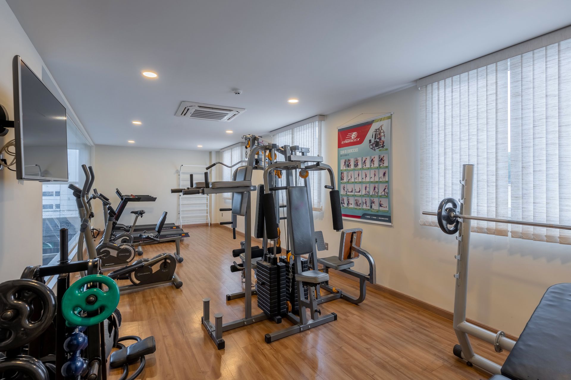 Interior de academia com aparelhos de ginástica, pesos e um pôster.