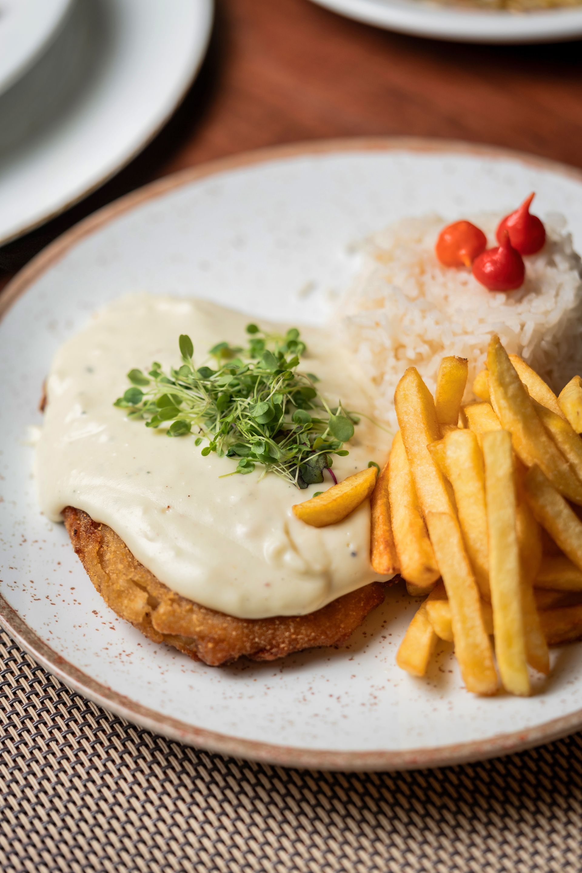 Prato de carne empanada com molho cremoso, arroz, batatas fritas e guarnição de pimentão vermelho.