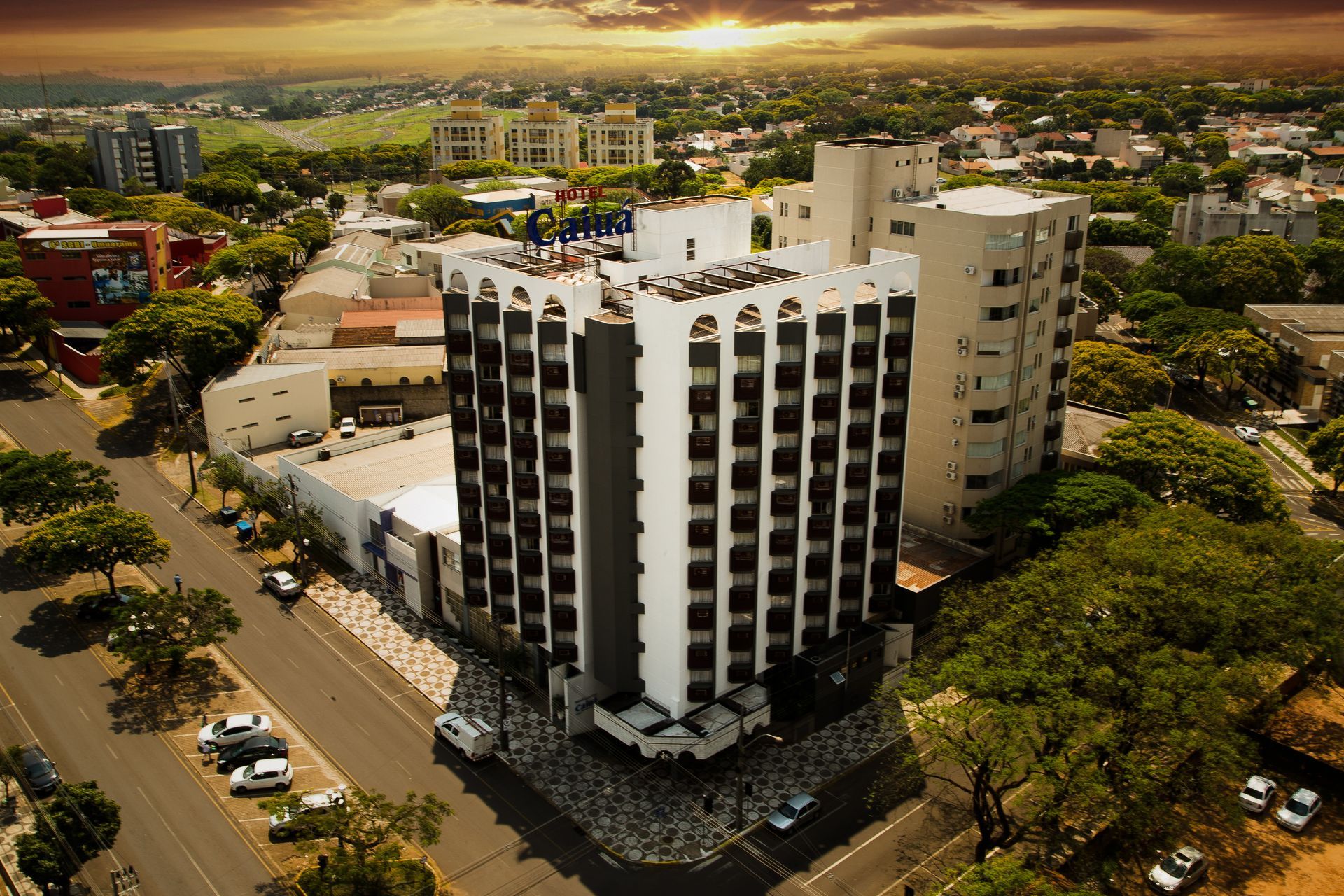 Hall de entrada com áreas de estar: sofás, poltronas e mesas redondas. Elevador e grandes janelas ao fundo.