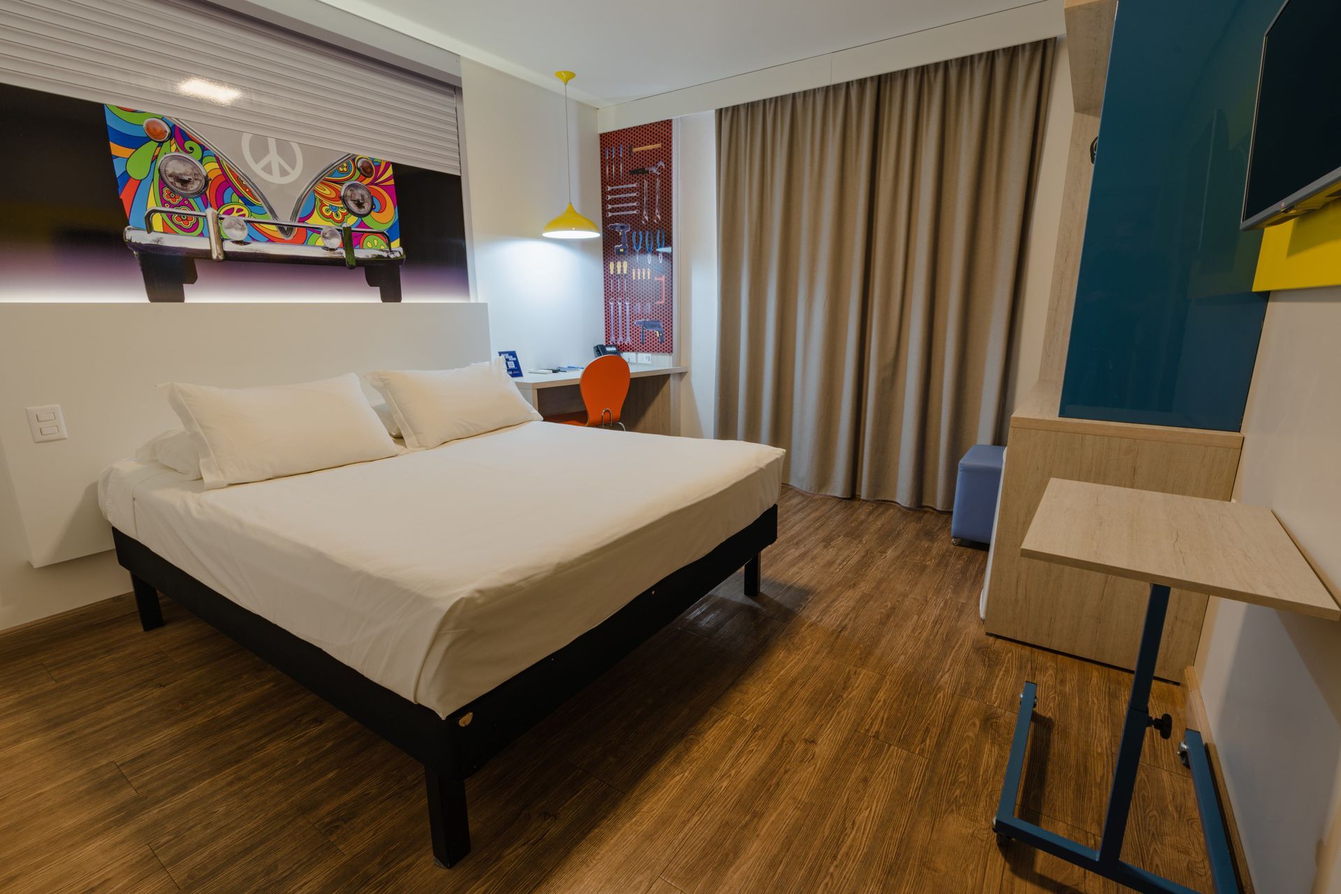 Quarto de hotel com cama de casal, escrivaninha, obras de arte e piso de madeira.