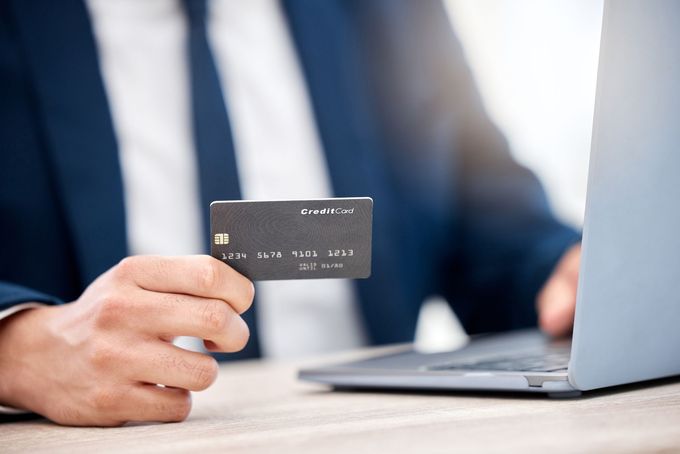 Man in suit holding a dark credit card, using a laptop for online transaction.