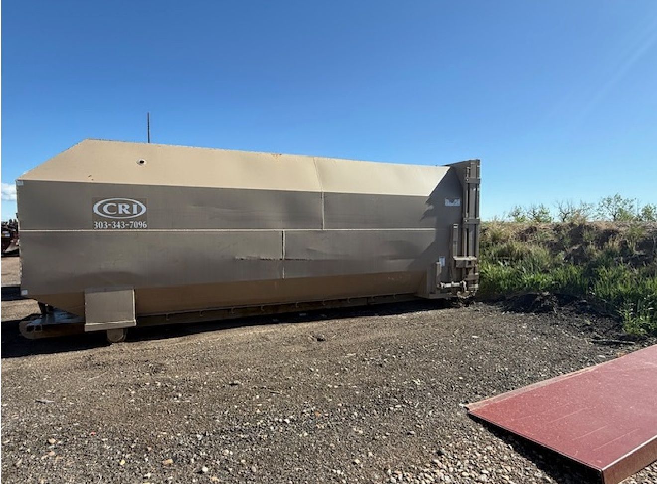 Large tan grain trailer with CRD logo parked on gravel, under a blue sky.