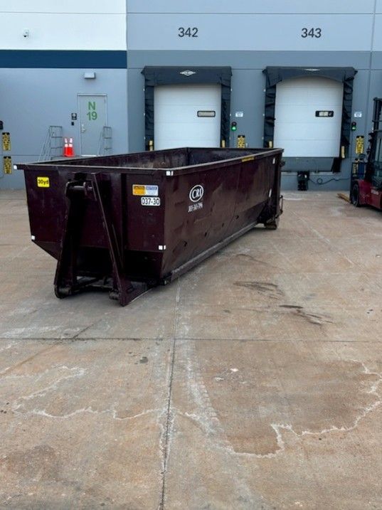 Dark maroon 30-yard roll-off dumpster on concrete pavement in front of warehouse loading docks