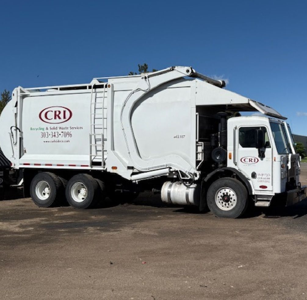 White CRI garbage truck parked on asphalt under a blue sky.