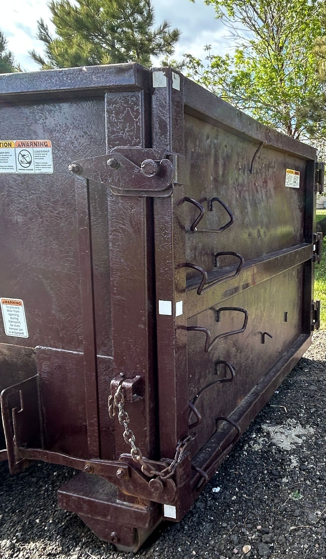Brown metal dumpster outdoors with rust marks, door open, and chains.