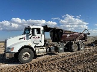 A roll-off truck delivering a dumpster on a dirt construction site.