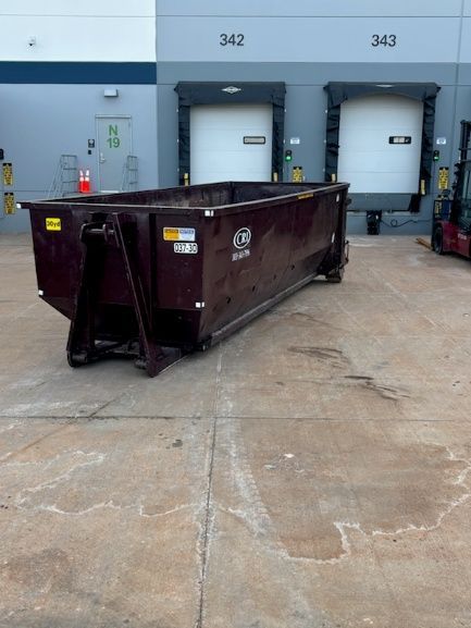 An dumpster placed on a concrete loading dock area in front of two white loading bay doors.