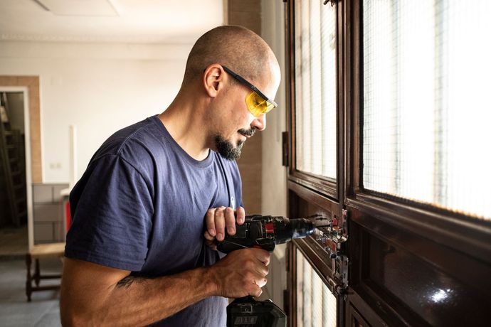Locksmith changes a lock at home with a battery drill. 