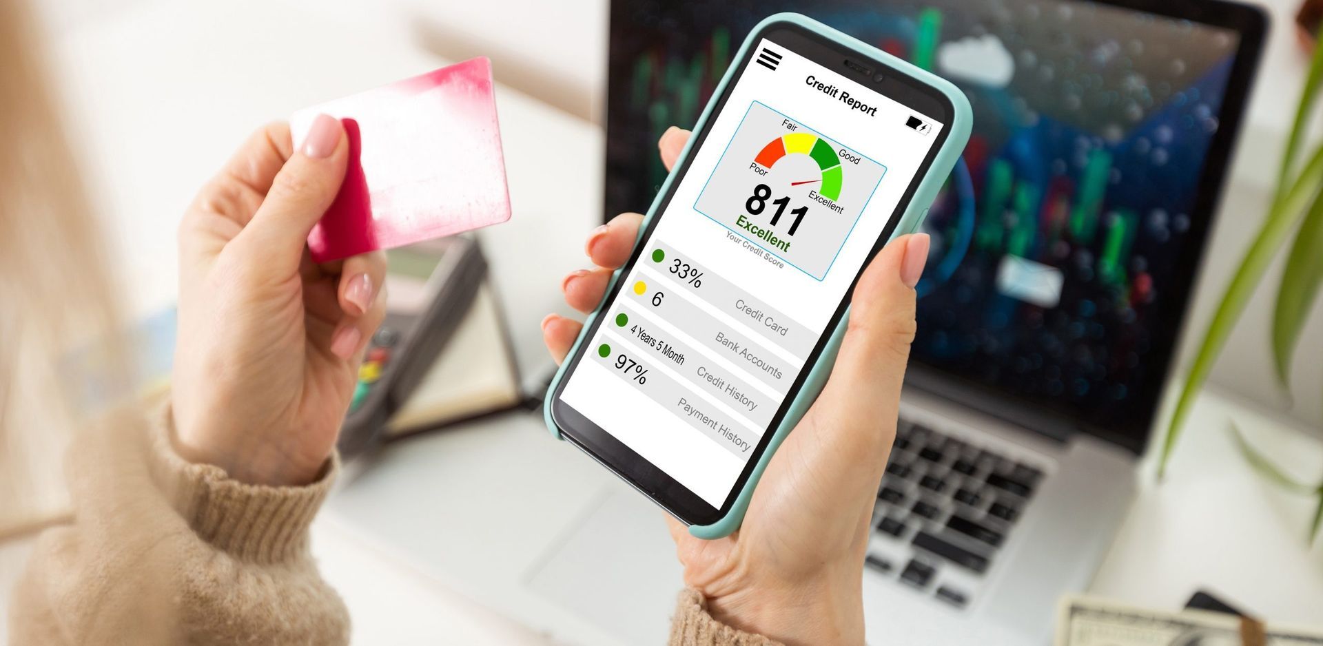 Una persona sostiene una tarjeta de crédito y un teléfono celular frente a una computadora portátil.