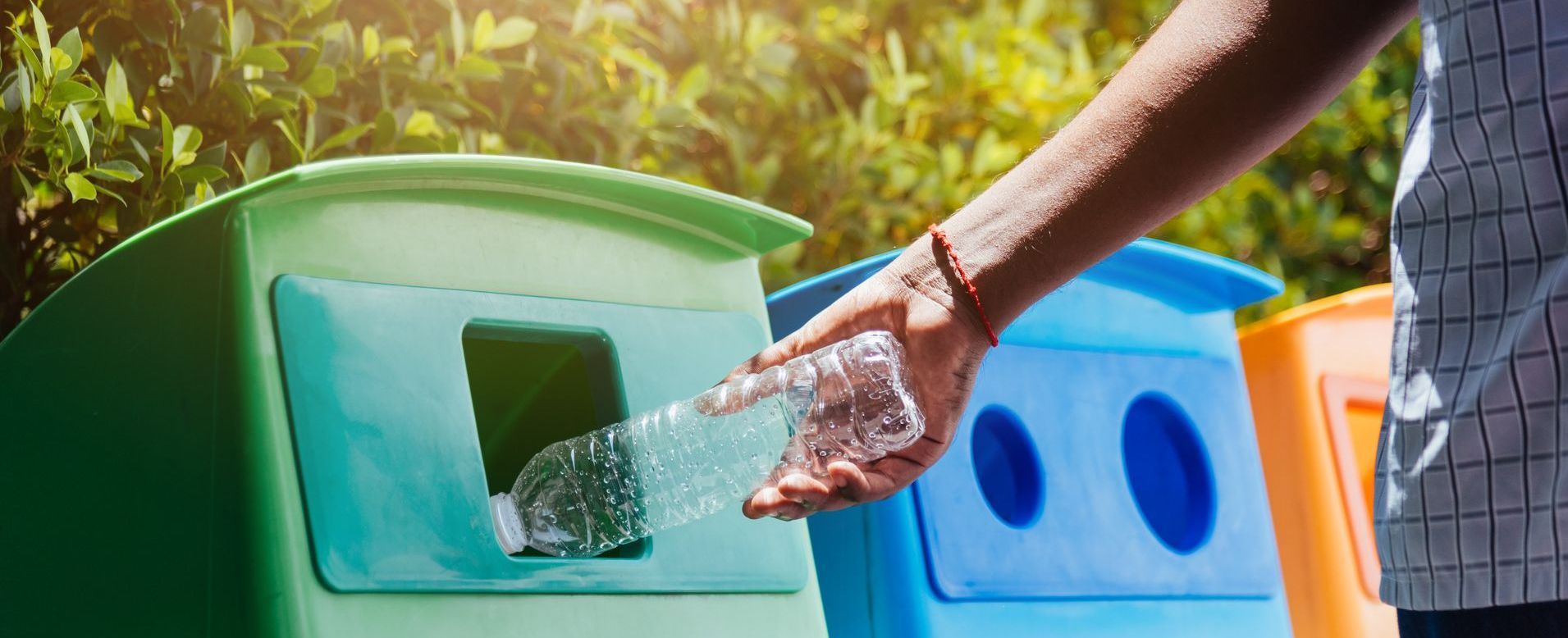 Una persona está tirando una botella de plástico a un contenedor de reciclaje.