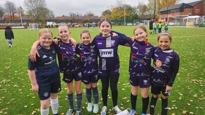 Six soccer players in purple uniforms posing on a grassy field after a match