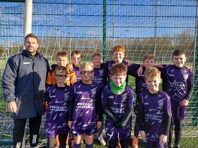 Soccer team and coach posing in purple uniforms in front of a goal net