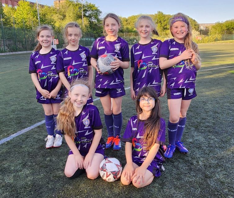 Youth soccer team in purple uniforms posing on a field, holding a ball and smiling.