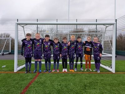 Youth soccer team in purple uniforms posing in front of a goal on a field