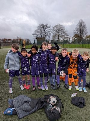 Youth soccer team in purple and orange uniforms posing on a field with a coach kneeling in front.