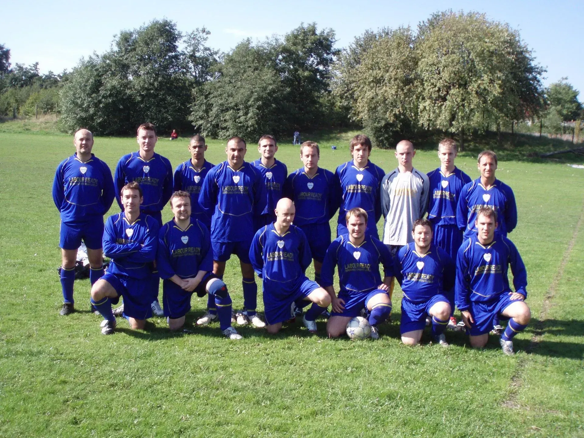Soccer team in blue uniforms posing on a grassy field with trees in the background