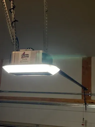 Ceiling-mounted garage door opener with a lit white light and black support arm.