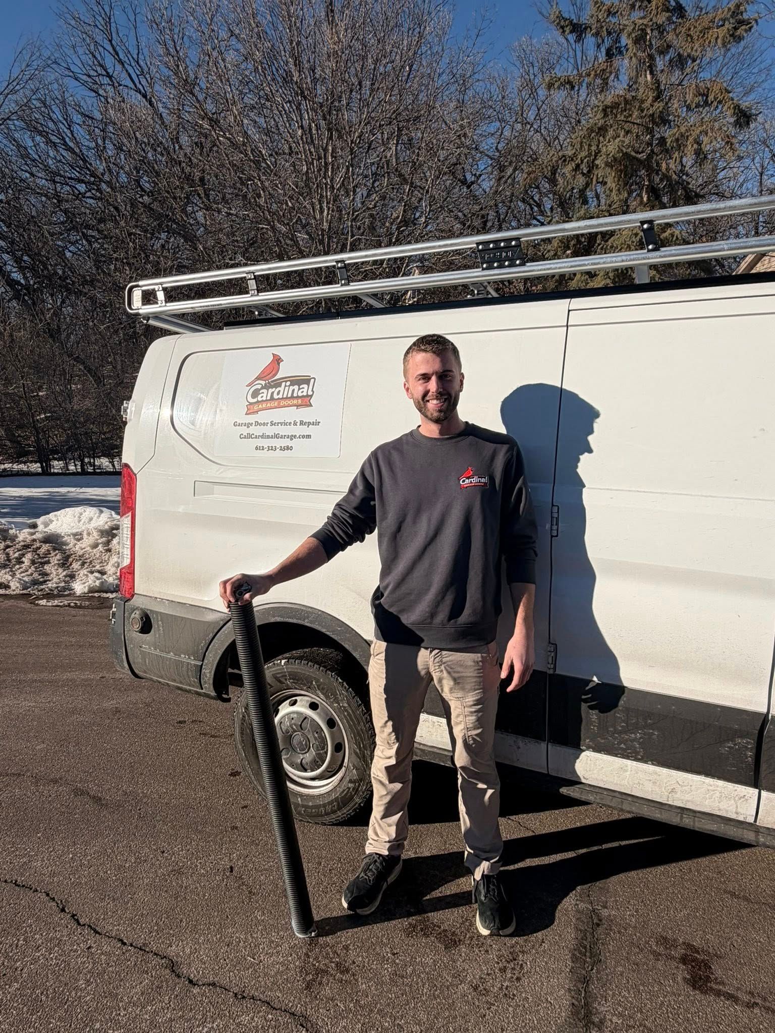 Man standing beside a white service van with a ladder on top, holding a tool in a sunny parking lot.