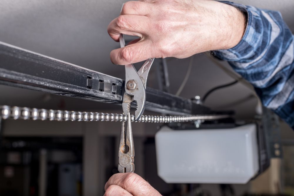 Hands using pliers to adjust a metal track or mechanism under a black surface