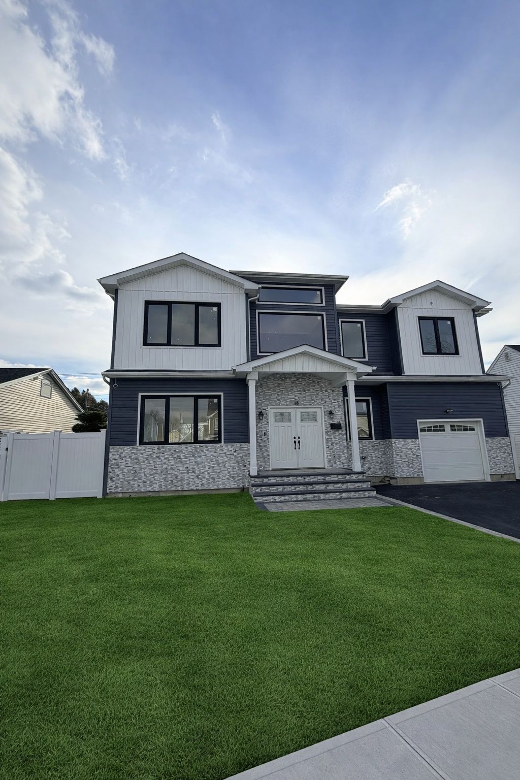 Two-story gray house with white trim, front steps, and a large green lawn under a cloudy sky