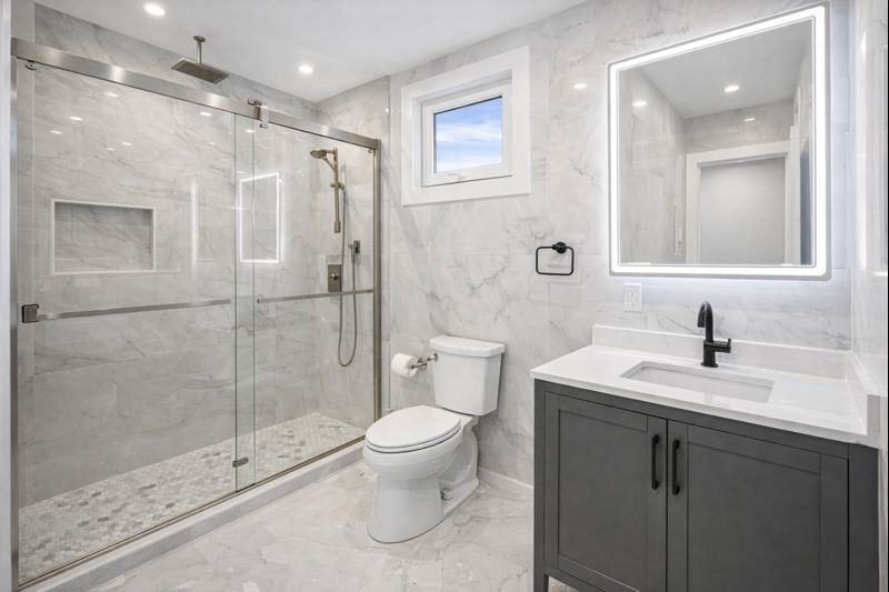 Modern gray bathroom with glass shower, toilet, and vanity sink