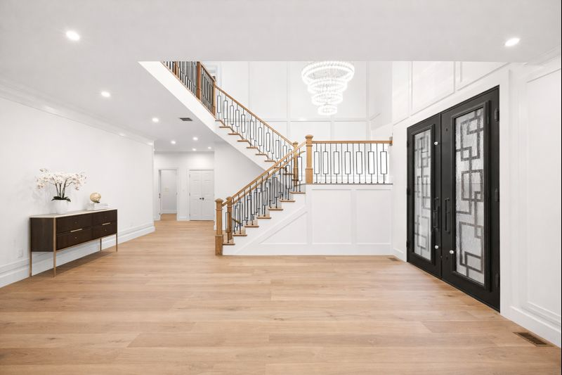 Bright modern foyer with hardwood floors, staircase, chandelier, and black front doors