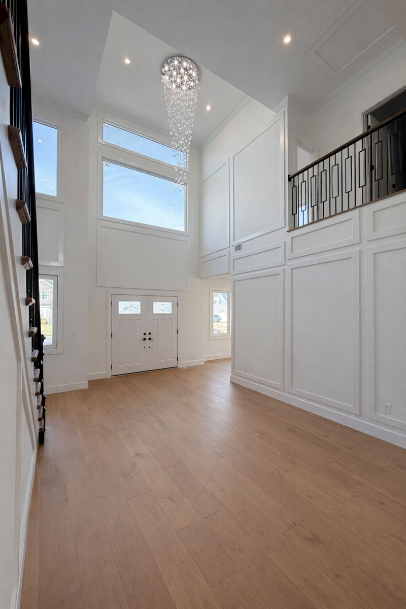 Bright two-story foyer with white walls, high windows, chandelier, and light wood floors