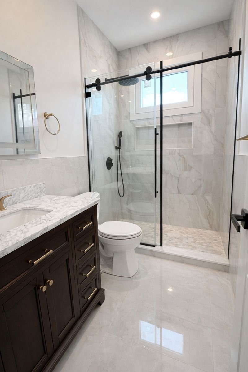 Modern bathroom with double glass shower doors, dark wood vanity, white tile, and a toilet