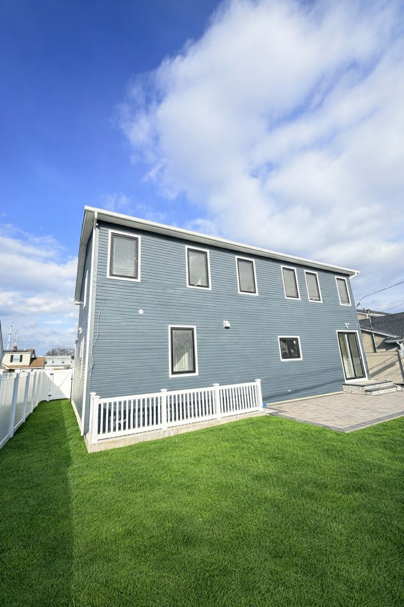 Gray two-story house with white trim, green lawn, and a partly cloudy blue sky.