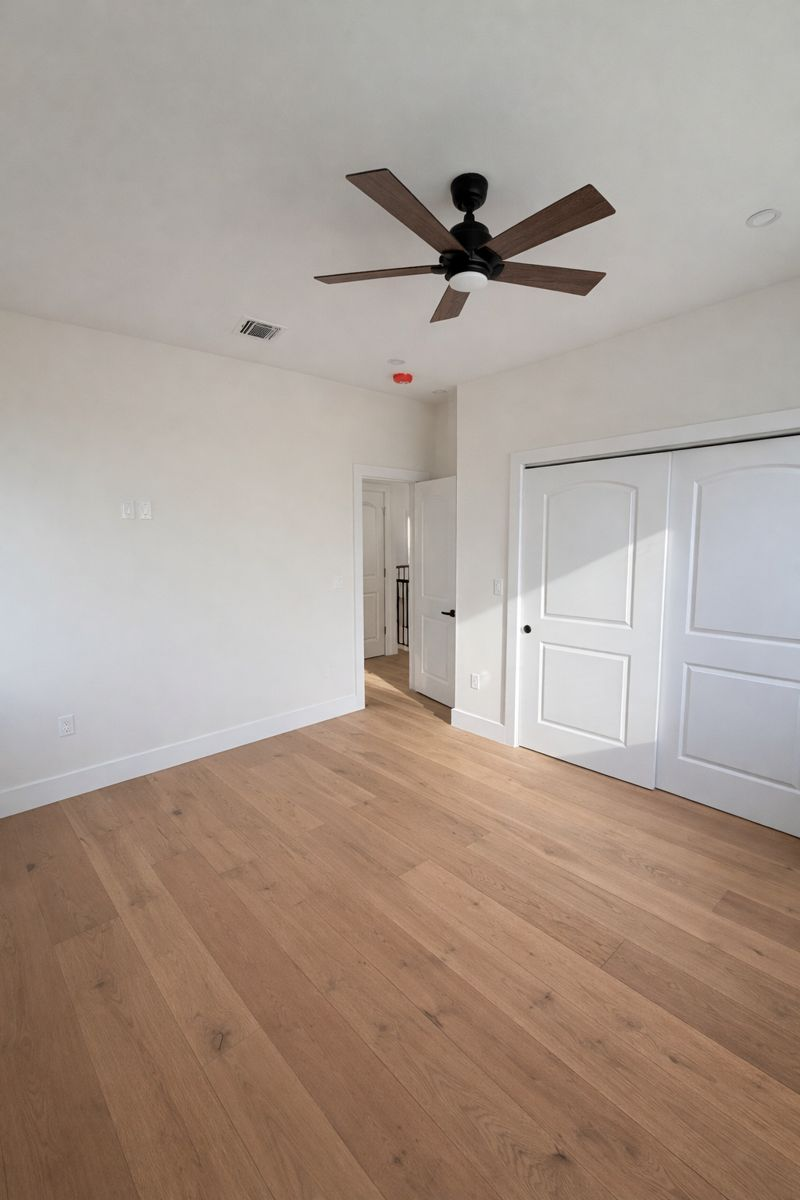 Empty white bedroom with wood floors, ceiling fan, and sliding closet doors